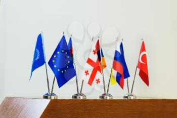 Miniature flags of European countries and the European Union flag on flagpoles on a wooden table.