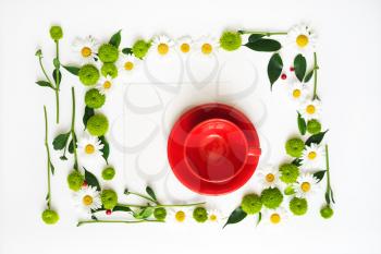 Paper and red cup for coffee or tea with wreath frame from chamomile and chrysanthemum flowers, ficus leaves and ripe rowan on white background. Overhead view. Flat lay.
