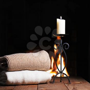 Warm woolen things and candle in candlestick near fireplace on wooden table. Winter and Christmas holiday concept.