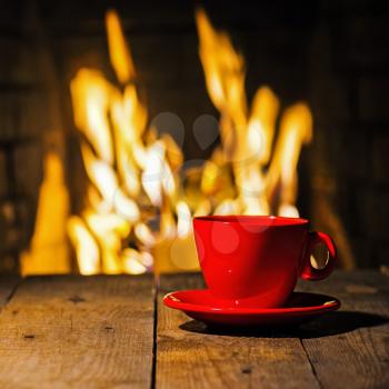 Red cup of coffee or tea on wooden table near  fireplace. Winter and Christmas holiday concept.