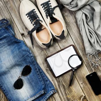 Set of travel items including scarf, sunglasses, sneakers, note book, magnifying glass, mobile phone and jeans. Overhead view. Flat lay.