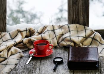 Red cup of coffee or tea with a metal spoon, a piece of sugar, photo album and loupe located on stylized wooden windowsill. Winter concept of comfort and relaxation.