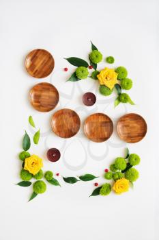 Wooden dishes with wreath frame from roses and chrysanthemum flowers, ficus leaves and ripe rowan on white background. Overhead view. Flat lay.
