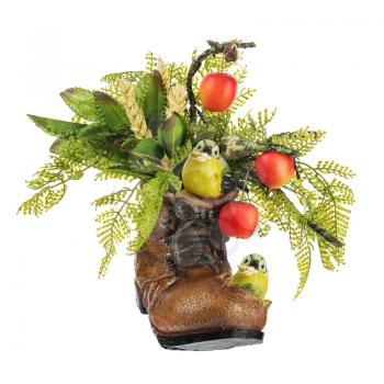 Table floral arrangement made of artificial flowers and fruits in stylized ceramic vase in the form of an old shoe with two birdies, holding in its beak ears of wheat isolated on white background.