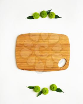 Wooden cutting board with decoration of chrysanthemum flowers and ficus leaves on white background. Overhead view. Flat lay.