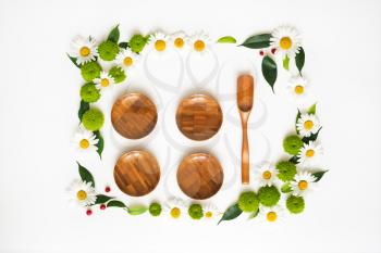 Wooden dishes with wreath frame from chamomile and chrysanthemum flowers, ficus leaves and ripe rowan on white background. Overhead view. Flat lay.