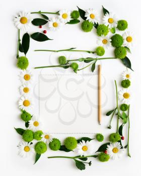 Paper and pencil with wreath frame from chamomile and chrysanthemum flowers, ficus leaves and ripe rowan on white background. Overhead view. Flat lay.
