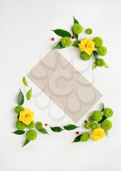Paper with wreath frame from roses, chamomile and chrysanthemum flowers, ficus leaves and ripe rowan on white background. Overhead view. Flat lay.