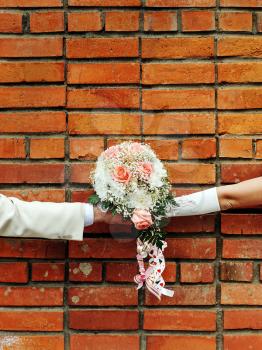 Two hands holding wedding bouquet against a brick wall.