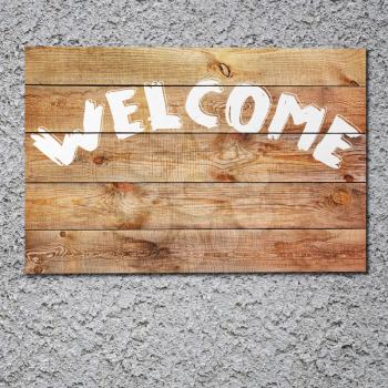 Vintage welcome wooden sign on gray stucco concrete wall.