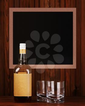Two glasses with ice for whiskey and bottle on dark wooden background.
