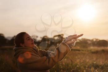 Outdoor fashion closeup portrait of pretty young woman with raised hands. Woman posing in autumn sunny sunset.