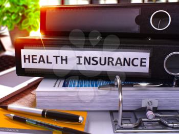 Black Ring Binder with Inscription Health Insurance on Background of Working Table with Office Supplies and Laptop. Health Insurance Business Concept on Blurred Background. 3D Render.