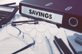 Savings - Office Folder on Background of Working Table with Stationery, Glasses, Reports. Business Concept on Blurred Background. Toned Image.