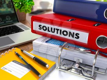 Red Ring Binder with Inscription Solutions on Background of Working Table with Office Supplies, Laptop, Reports. Toned Illustration. Business Concept on Blurred Background.