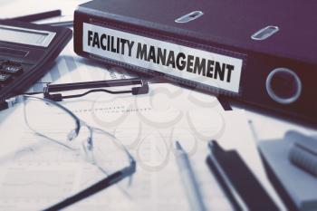 Facility Management - Office Folder on Background of Working Table with Stationery, Glasses, Reports. Business Concept on Blurred Background. Toned Image.