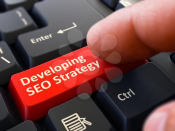 Developing SEO Strategy Button. Male Finger Clicks on Red Button on Black Keyboard. Closeup View. Blurred Background.