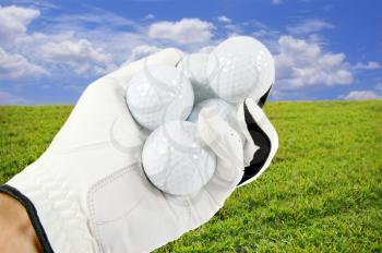 Royalty Free Photo of a Hand Holding Golf Balls Against a Blue Sky and Green Grass