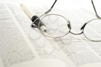 Reading glasses and pen in a dictionary with the word Education