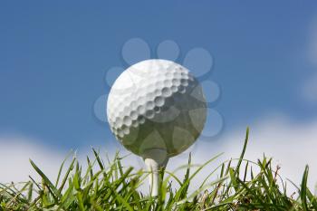 Close up shot of a golf ball with a low angle showing green grass and blue sky