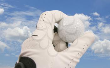 Hand holding a golf ball against a blue sky