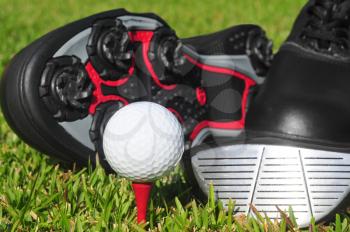 Golf ball on a tee with a club and golf shoes in the background