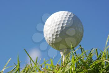 Golf ball on grass against a blue sky and white clouds 