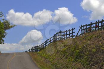 Panoramic shot of a mountain road with a fence and a blue sky