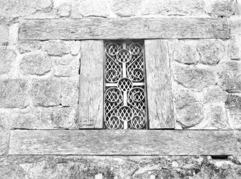 Old stone wll with a wooden frame and small welded iron window in black and white