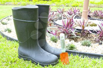 Black rubber boots and gardening tool in a house garden
