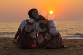 The young couple sitting on a sea beach and watching the beautiful sunset.