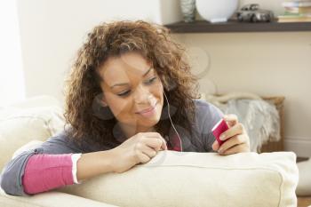Woman Listening To MP3 Player On Headphones Relaxing Sitting On Rug At Home