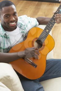 Young Man Relaxing Sitting On Sofa Playing Acoustic Guitar
