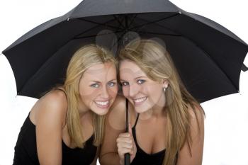Studio shot of two beautiful young women sharing an umbrella