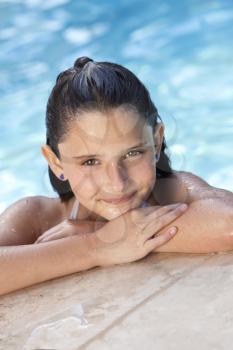 A cute happy young girl child relaxing on the side of a swimming pool 