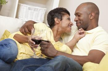 A happy African American man and woman couple in their thirties sitting at home together smiling and drinking glasses of red wine.