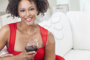 A beautiful mixed race African American girl or young woman wearing a red dress looking happy and drinking red wine