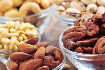 Many glass bowls of almonds walnuts pistachios and pine nuts