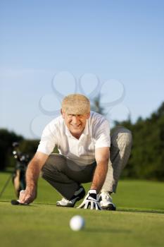 Senior man playing golf aiming for the hole, it is a wonderful clear summer late afternoon, the colors are very vivid