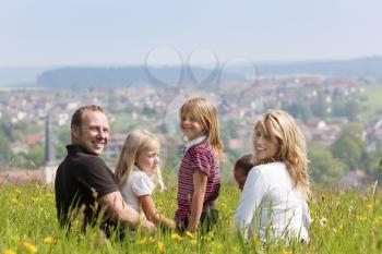 Very happy family with three kids sitting in a meadow with dandelion in the summer sun
