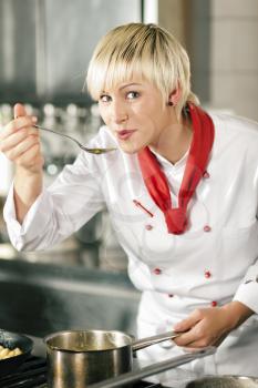 Female chefs in a restaurant or hotel kitchen cooking delicious food, tasting the half finished dish with a spoon