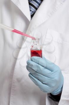 Scientist, chemist, pharmacist or laboratory technician adding a pipetted sample to a laboratory bottle. Focus to hand, pipet and bottle