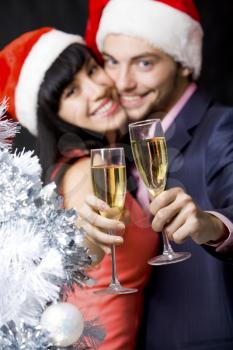 Image of happy couple stretching champagne flutes with silver tree at foreground