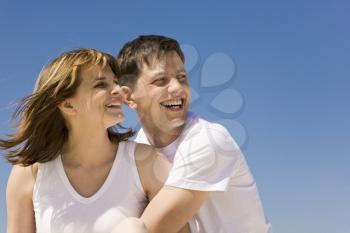 Portrait of cheerful couple looking aside against blue sky