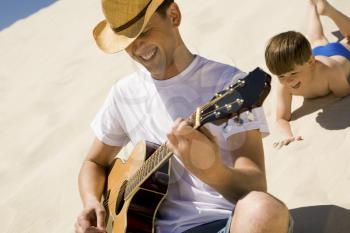 Portrait of happy man in cowboy hat playing the guitar with his son at background