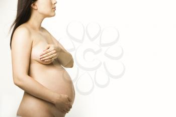 Pregnant nude woman standing in profile and touching her tummy