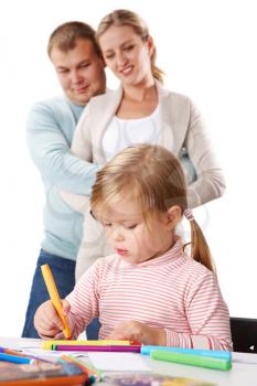 Photo of adorable girl drawing with highlighters with her parents behind