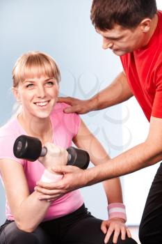 Photo of active girl lifting dumbbell in the sports club with her instructor near by