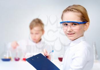 A little girl in protective glasses making notes and looking at camera