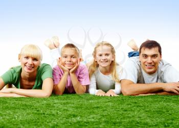 Portrait of happy family lying on green lawn and looking at camera 